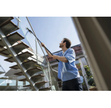 Een man reinigt een glazen balustrade van een buiten-trap van metaal en hout met een telescoopwisser.