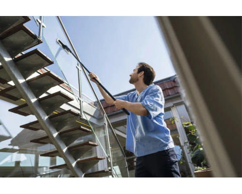 Een man reinigt een glazen balustrade van een buiten-trap van metaal en hout met een telescoopwisser.