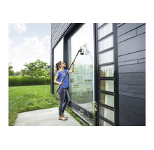 Vrouw reinigt een hoog glazen pui aan een modern huis met een accu raamwisser met verlengset.
