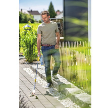 Een man gebruikt een gas onkruidbrander op een bestraat terras in de tuin om onkruid tussen de tegels te verwijderen.