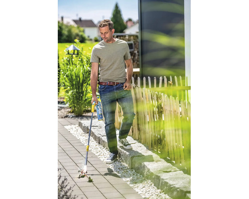 Een man gebruikt een gas onkruidbrander op een bestraat terras in de tuin om onkruid tussen de tegels te verwijderen.