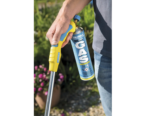 Een persoon houdt een Gloria Thermoflamm gasbrander met gascartouche vast in de tuin voor onkruidbestrijding.