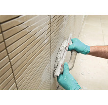 Handwerker met handschoenen voegt een betegelde muur met een voegspaan.