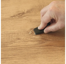 Hand bewerkt een houten oppervlak met een schraper om materiaal te verwijderen of een reparatieplek glad te maken.