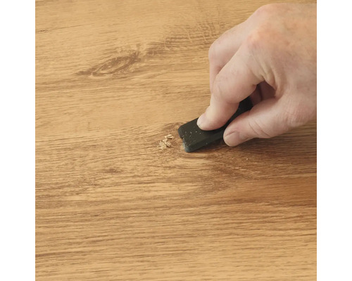 Hand bewerkt een houten oppervlak met een schraper om materiaal te verwijderen of een reparatieplek glad te maken.