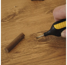 Hand die een wassmelter boven een houten oppervlak houdt naast een wasstaaf voor het repareren van vloeren