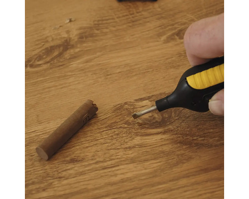 Hand die een wassmelter boven een houten oppervlak houdt naast een wasstaaf voor het repareren van vloeren
