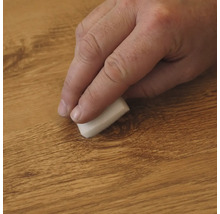 Hand wrijft met een kleine spons over een houten oppervlak voor onderhoud of reiniging