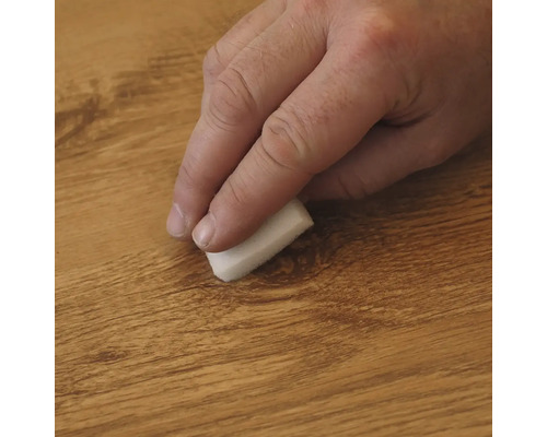 Hand wrijft met een kleine spons over een houten oppervlak voor onderhoud of reiniging