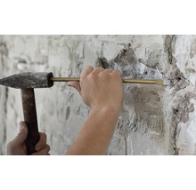 Handwerker aan het werk met een bankhamer en een beitel voor het verwijderen van metselwerk aan een gepleisterde muur.