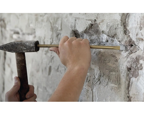 Handwerker aan het werk met een bankhamer en een beitel voor het verwijderen van metselwerk aan een gepleisterde muur.