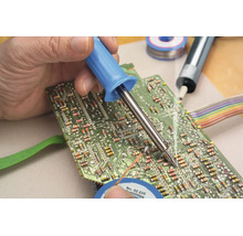 Een hand soldeert een elektronisch component op een groene printplaat met een soldeerbout.