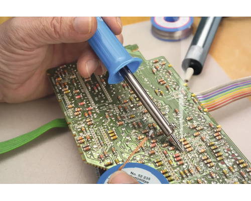 Een hand soldeert een elektronisch component op een groene printplaat met een soldeerbout.