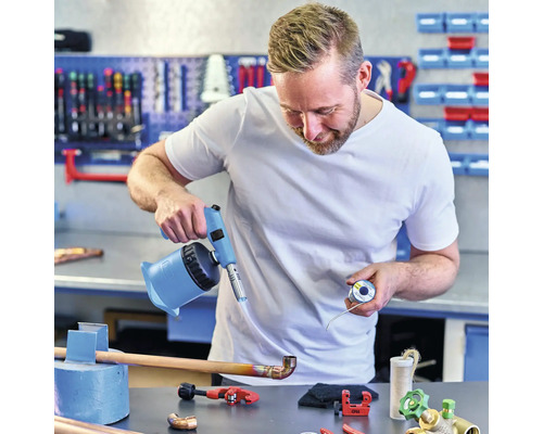 Een vakman soldeert een koperen pijp met een soldeerbrander in een werkplaats.