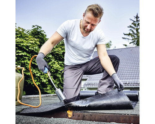 Vakman die bitumen dakbedekking vastbrandt met een gasbrander op een plat dak.