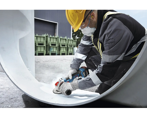 Vakman met beschermende kleding gebruikt een Bosch accu haakse slijper voor het bewerken van een groot werkstuk op een bouwplaats.