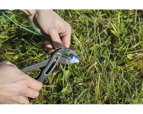 Een persoon gebruikt een waterpomptang om een begrenzingskabelverbinder voor een robotmaaier in het gras te monteren.