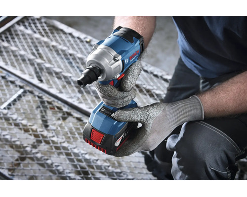 Persoon met veiligheidshandschoenen houdt een Bosch accu slagmoersleutel 18 volt boven een metalen rooster.