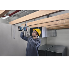 Vakman met veiligheidshelm en bril monteert een houten plafondconstructie met een accuboormachine op een bouwplaats.