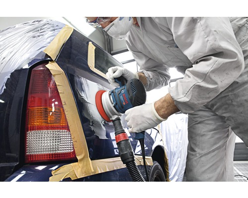 Een arbeider schuurt een auto met een schuurmachine in een werkplaats.