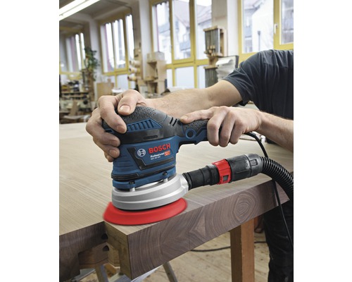 Een persoon schuurt hout met een excentrische schuurmachine van Bosch.