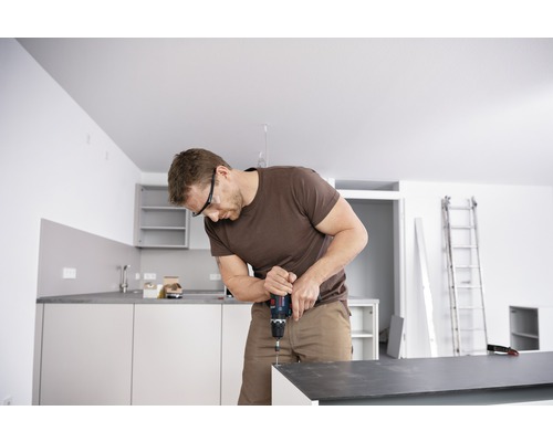 Man met veiligheidsbril werkt met accuboormachine in de keuken