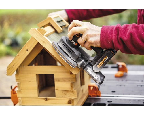 Iemand schuurt een vogelhuisje met een excentrische schuurmachine van Worx.