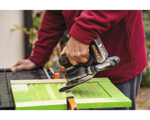 Ambachtsman schuurt groene luiken met een Worx accu-multischuurmachine