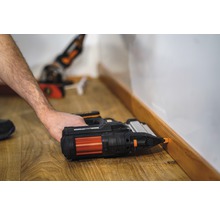 Iemand bevestigt een plint met een accuspijkermachine aan een muur.