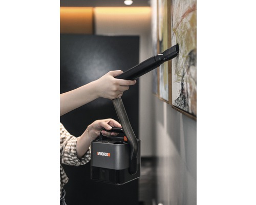 Een persoon reinigt een schilderij aan de muur met een draagbare Worx stofzuiger.