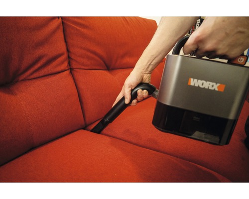 Persoon stofzuigt een bank met een draadloze stofzuiger van Worx