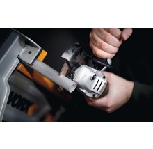 Iemand snijdt een buis met een haakse slijper in een werkplaats. Worx logo.
