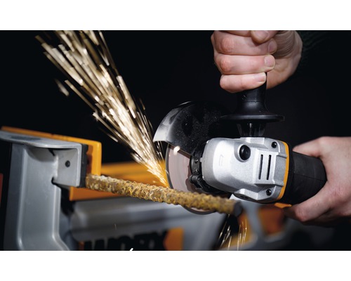 Een persoon snijdt een staaf in een bankschroef met een haakse slijper, waardoor vonken ontstaan.