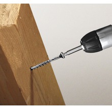 Een schroevendraaier schroeft een schroef in een stuk hout