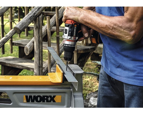 Een persoon boort met een accuboormachine een gat in een stuk metaal dat op een werkbank ligt.