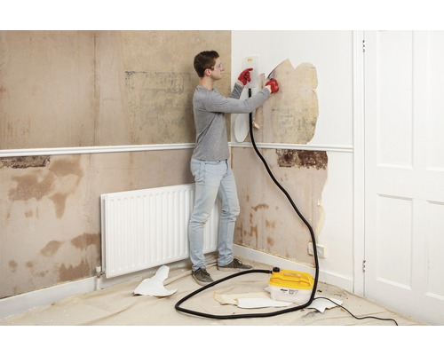 Een man verwijdert behang met een behangafstomer in een kamer.