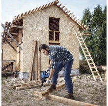 Ambachtsman boort met een boormachine een gat in een houten balk voor een huis in aanbouw.