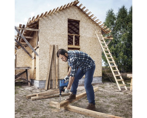 Ambachtsman boort met een boormachine een gat in een houten balk voor een huis in aanbouw.