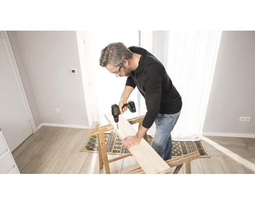 Man boort een gat in een houten plank met een accuboormachine die op een werkbank ligt.