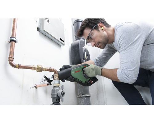 Een vakman gebruikt een reciprozaag van Bosch om een koperen pijp door te zagen. Hij draagt beschermende kleding zoals een veiligheidsbril en handschoenen.