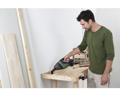 Een man stofzuigt een houten werkbank met een draadloze handstofzuiger.