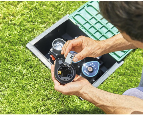 Man plaatst batterij in irrigatiecomputer in een schacht in het gazon