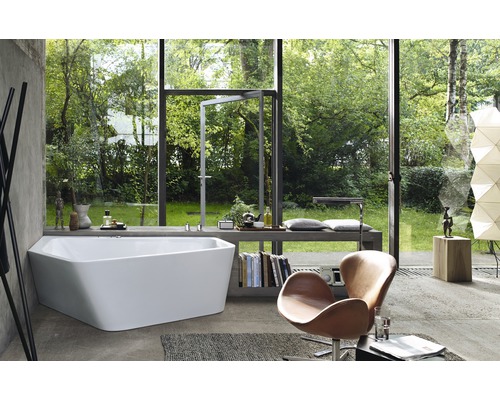 Lichte badkamer met ligbad voor raam met uitzicht op de tuin, fauteuil en boeken