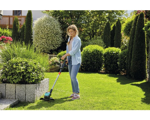 Vrouw maait gazon met een grastrimmer in de tuin.