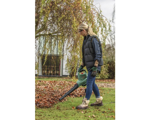 Vrouw gebruikt een bladblazer in de tuin om herfstbladeren te verwijderen.