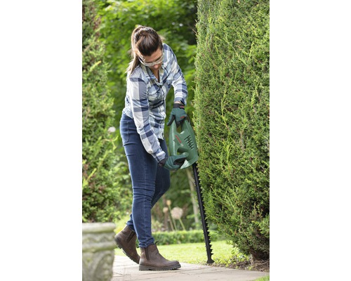 Vrouw snoeit haag met een heggenschaar van Bosch in de tuin.