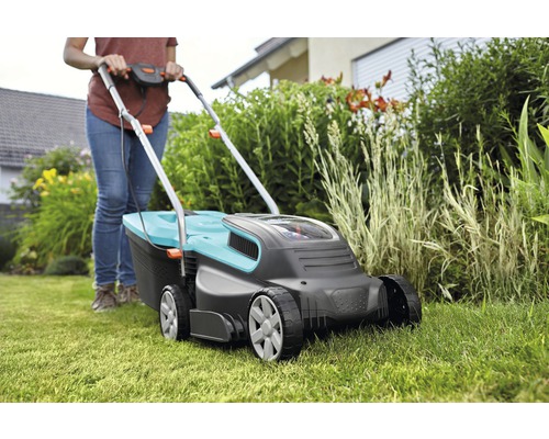 Vrouw bedient grasmaaier in de tuin.