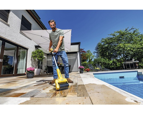 Man reinigt stenen terras met een terrasreinigingsborstel in de buurt van een zwembad.