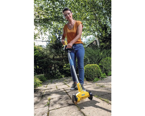 Vrouw gebruikt een voegenkrabber om onkruid te verwijderen op een trottoir.