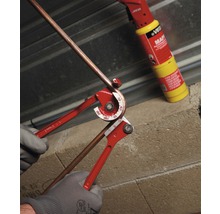 Pijpenbuiger in gebruik voor het buigen van een koperen pijp met een soldeerlamp op de achtergrond